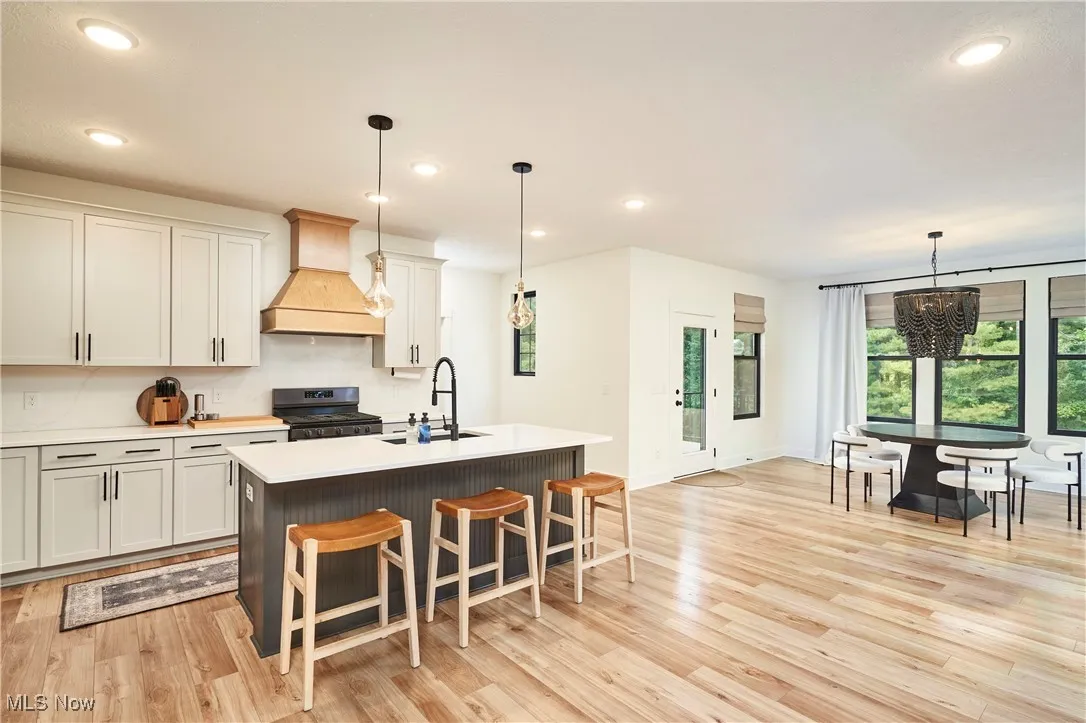 Kitchen with recessed lighting, custom exhaust hood, a breakfast bar area, stainless steel stove, and decorative light fixtures