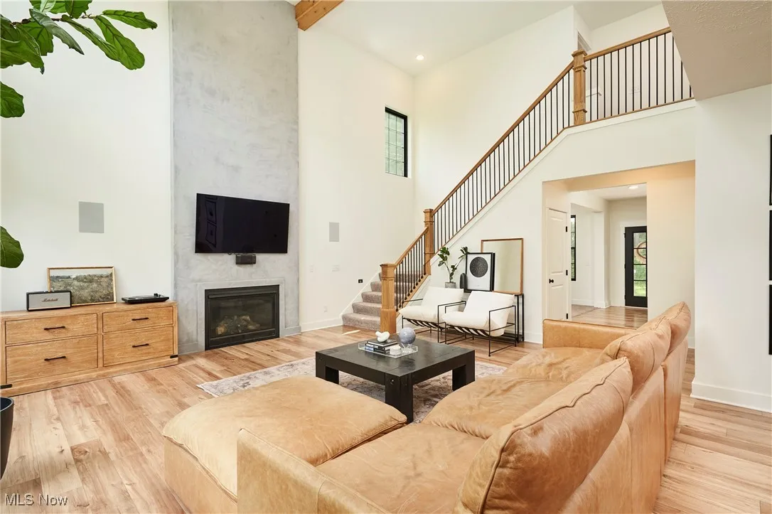 Living room featuring a fireplace, light wood-style flooring, beam ceiling, a high ceiling, and stairway