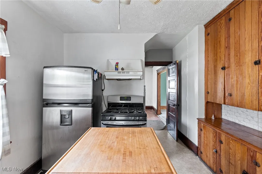 Kitchen with appliances with stainless steel finishes, a textured ceiling, butcher block countertops, under cabinet range hood, and brown cabinetry