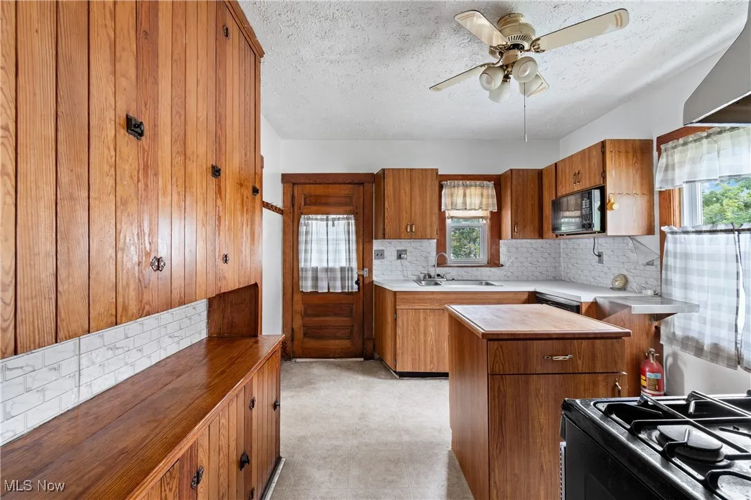 Kitchen featuring backsplash, brown cabinetry, black appliances, extractor fan, and a textured ceiling