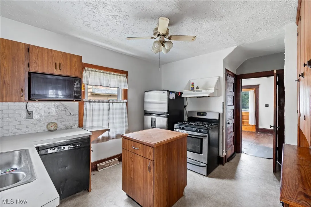 Kitchen featuring brown cabinetry, black appliances, a center island, light countertops, and a textured ceiling