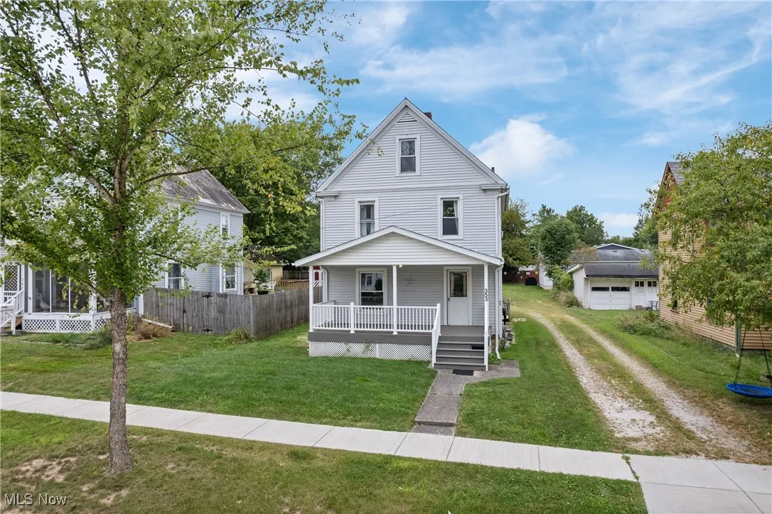 Traditional style home with driveway, covered porch, a front yard, an outdoor structure, and a detached garage