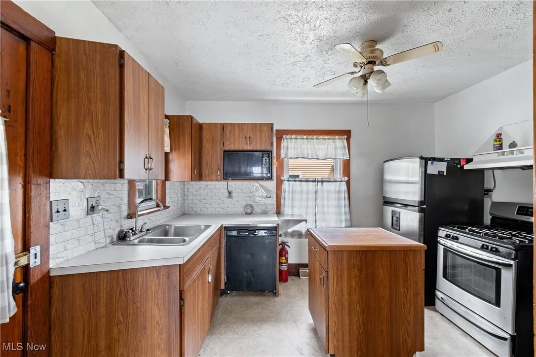 Kitchen featuring a center island, black appliances, brown cabinetry, backsplash, and a textured ceiling