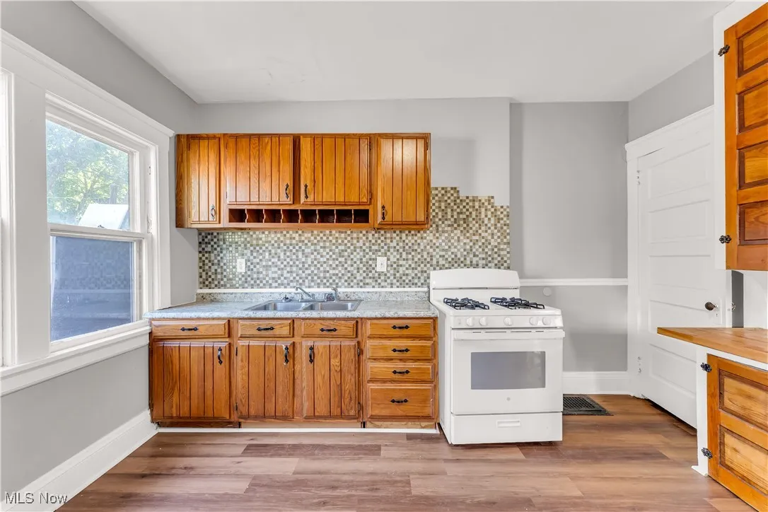 Kitchen with white range with gas cooktop, tasteful backsplash, brown cabinets, and light wood-style floors