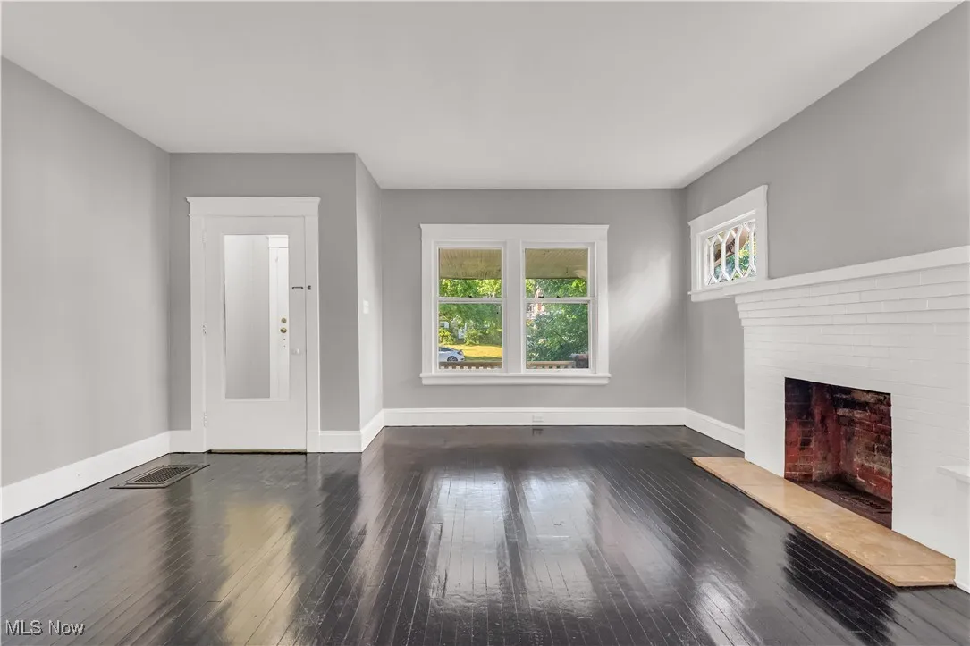 Unfurnished living room with dark wood-style flooring and a brick fireplace