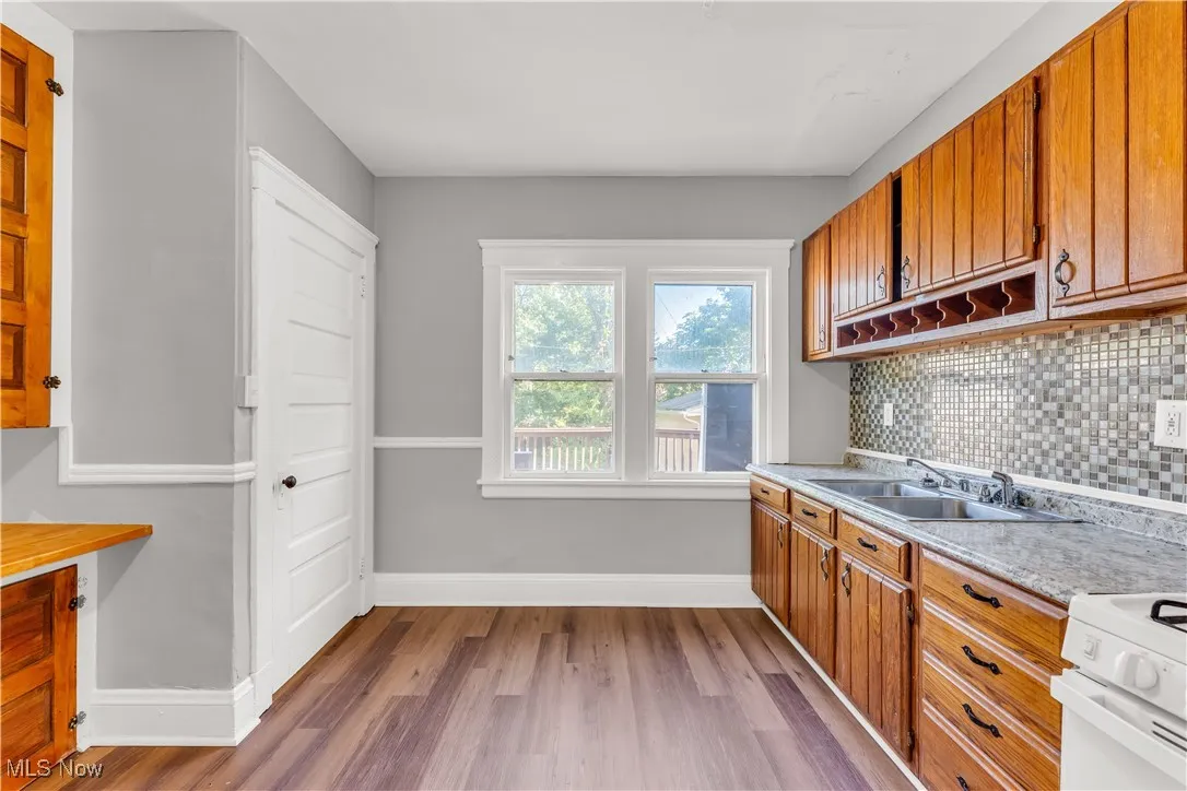 Kitchen featuring light countertops, brown cabinetry, light wood-type flooring, white range with gas stovetop, and decorative backsplash