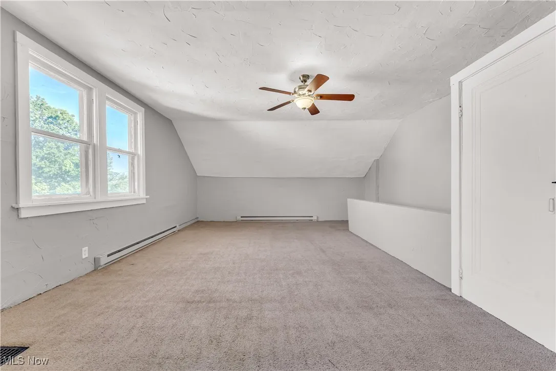 Additional living space featuring light carpet, vaulted ceiling, baseboard heating, a textured ceiling, and a ceiling fan