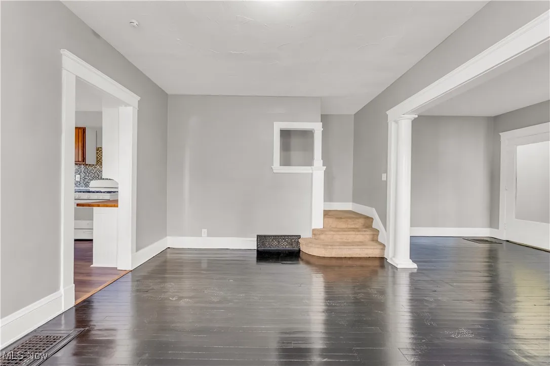 Unfurnished living room with dark wood finished floors, ornate columns, and stairs