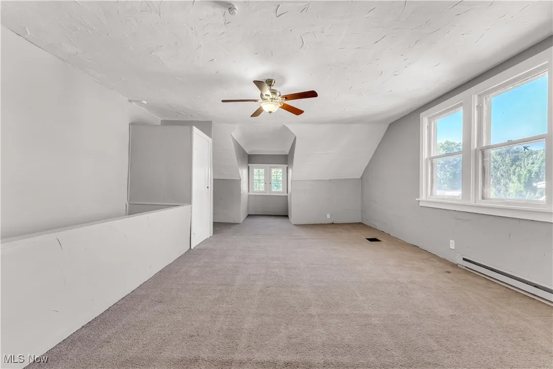 Bonus room with light colored carpet, lofted ceiling, ceiling fan, and a textured ceiling