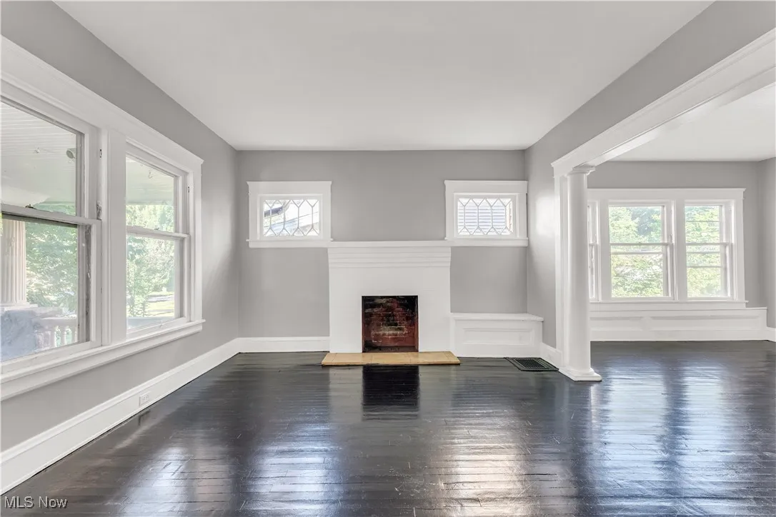 Unfurnished living room with dark wood-style flooring, a fireplace with raised hearth, and ornate columns
