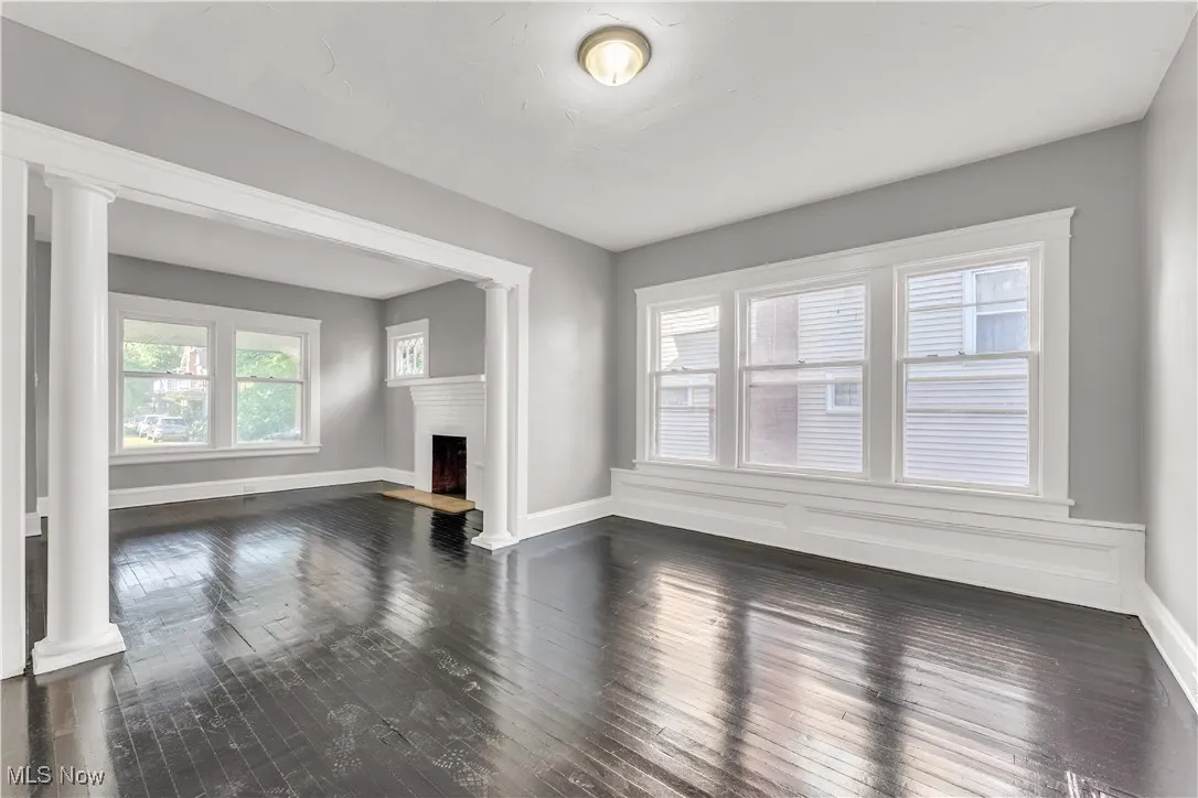 Unfurnished living room featuring ornate columns, dark wood-style floors, healthy amount of natural light, and a fireplace