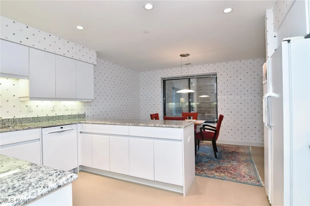 Kitchen with white cabinetry, white appliances, hanging light fixtures, modern cabinets, and light stone countertops