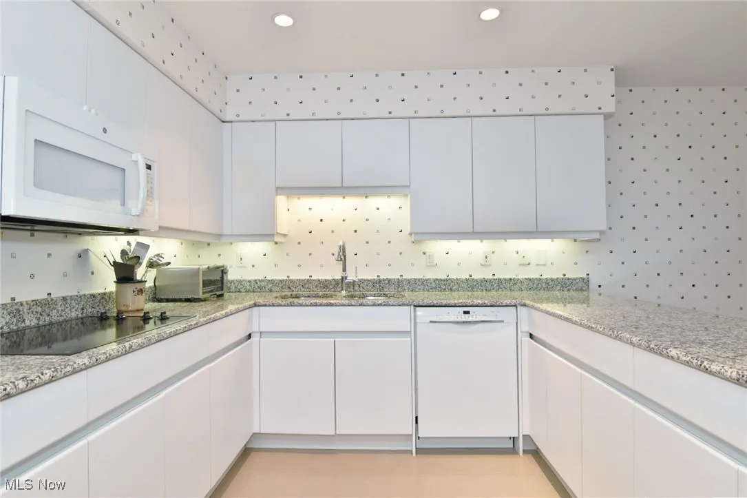 Kitchen with white cabinetry, white appliances, light stone counters, and recessed lighting
