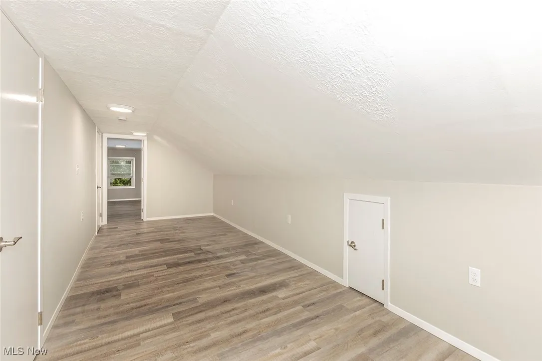 Additional living space featuring light wood-style floors, a textured ceiling, and lofted ceiling