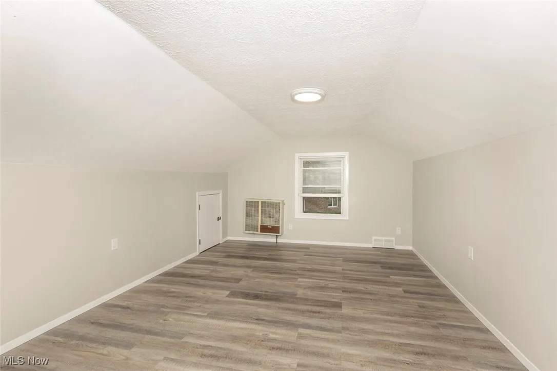 Additional living space featuring a textured ceiling, lofted ceiling, light wood-style floors, and heating unit