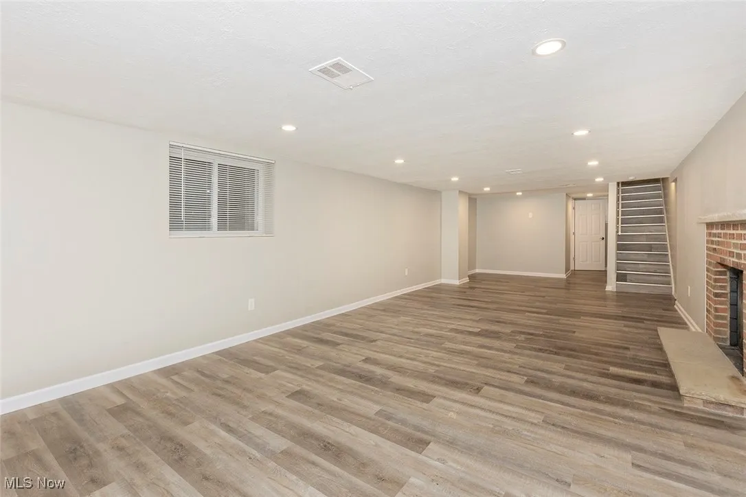 Finished basement with light wood finished floors, recessed lighting, a fireplace, and stairs