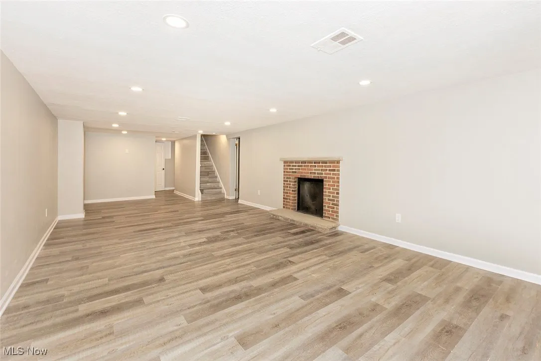 Unfurnished living room featuring a brick fireplace, stairway, light wood finished floors, and recessed lighting