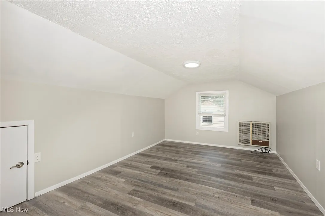 Bonus room with vaulted ceiling, a textured ceiling, heating unit, and wood finished floors