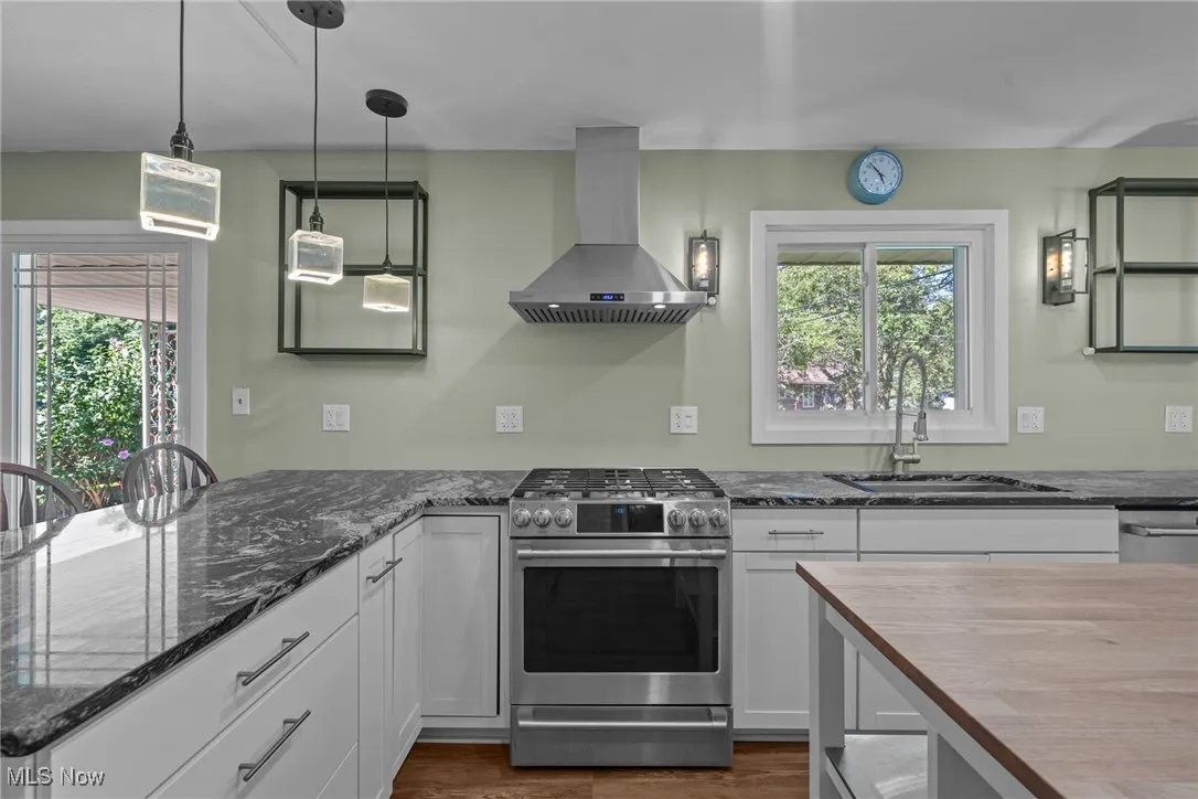 Kitchen with stainless steel appliances, hanging light fixtures, island exhaust hood, butcher block countertops, and white cabinetry