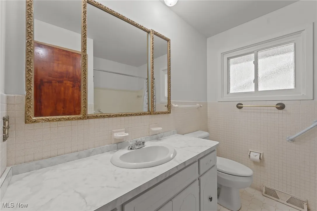 Full bathroom featuring tile walls, vanity, wainscoting, light tile patterned floors, and a shower with shower curtain