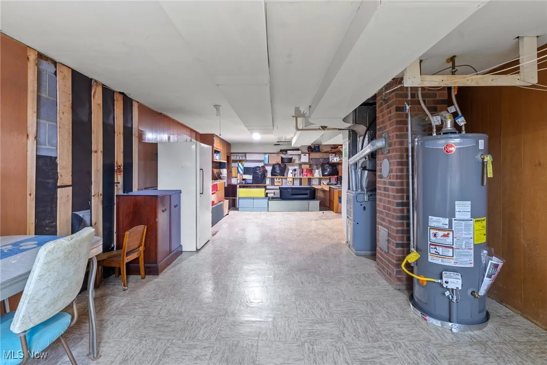 Finished below grade area featuring light floors, wood walls, gas water heater, and freestanding refrigerator
