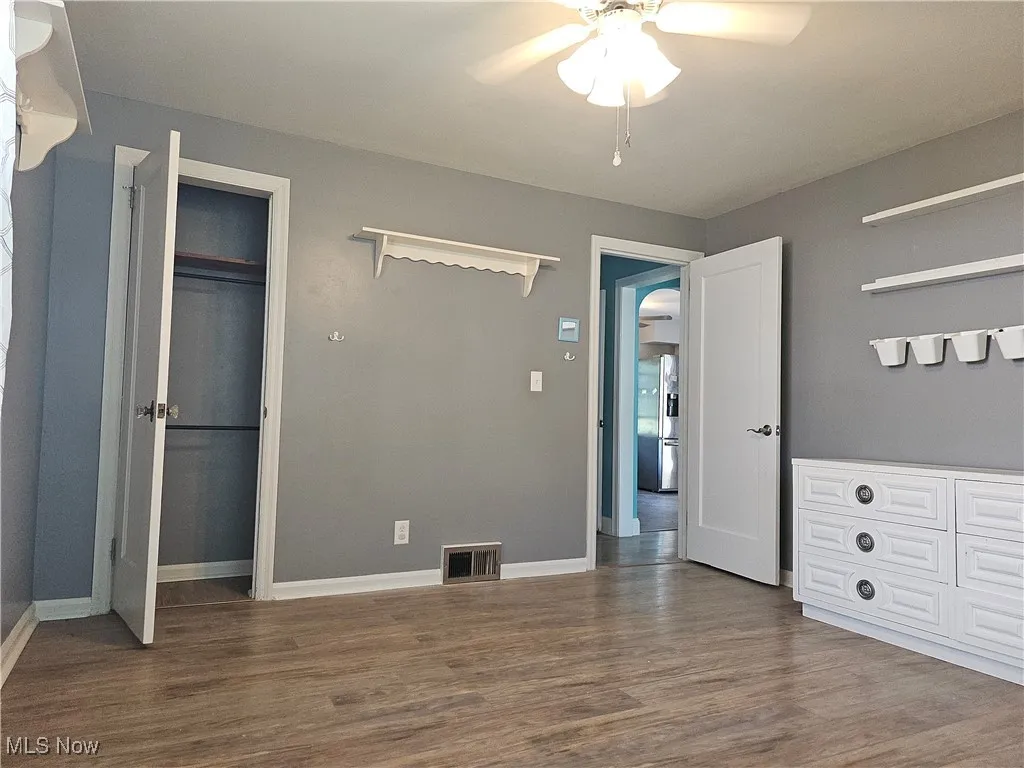 Unfurnished bedroom featuring dark wood-style floors, stainless steel refrigerator with ice dispenser, and a ceiling fan