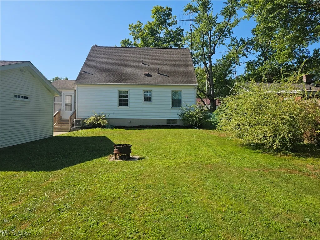 Rear view of property with roof with shingles, a yard, and an outdoor fire pit