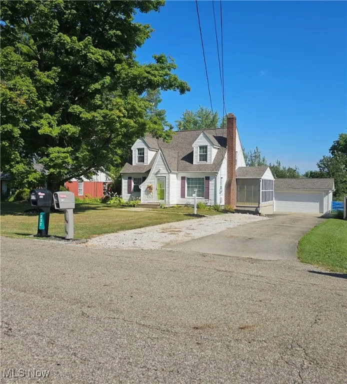 Cape cod-style house with a chimney, a front lawn, an outbuilding, and concrete driveway