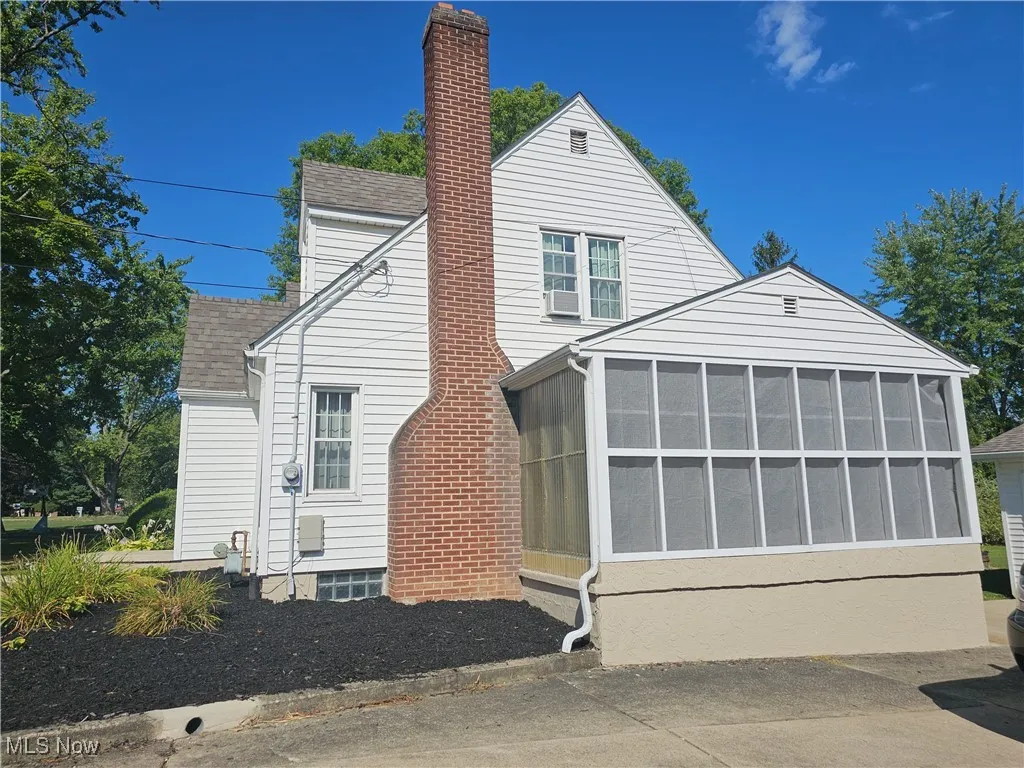 View of home's exterior featuring a shingled roof, a sunroom, and a chimney