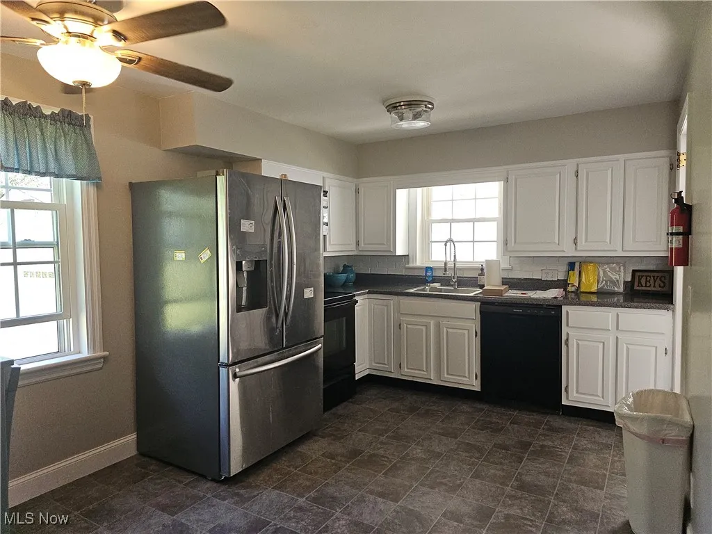 Kitchen with black appliances, white cabinetry, dark countertops, ceiling fan, and stone finish flooring