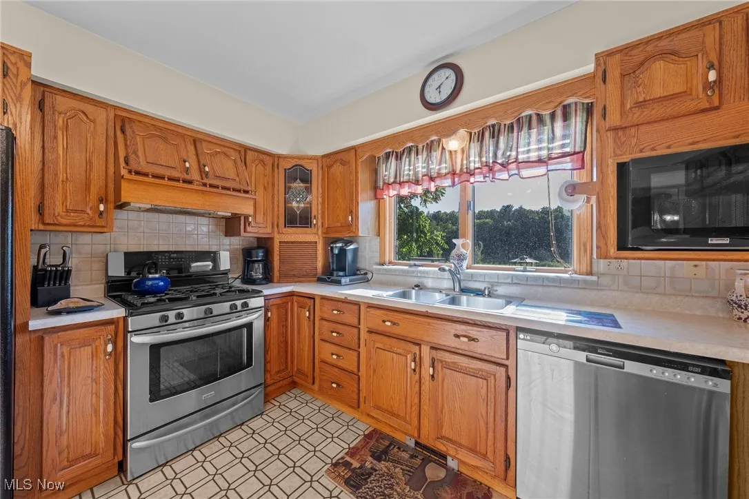 Kitchen with appliances with stainless steel finishes, light countertops, tasteful backsplash, brown cabinetry, and custom exhaust hood