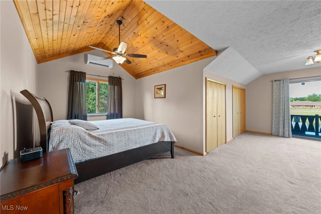 Carpeted bedroom with lofted ceiling, multiple windows, wooden ceiling, a wall unit AC, and a ceiling fan