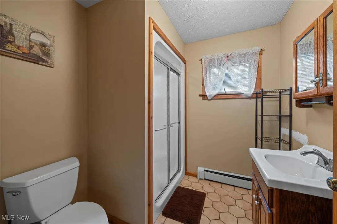 Bathroom featuring baseboard heating, a stall shower, vanity, and a textured ceiling