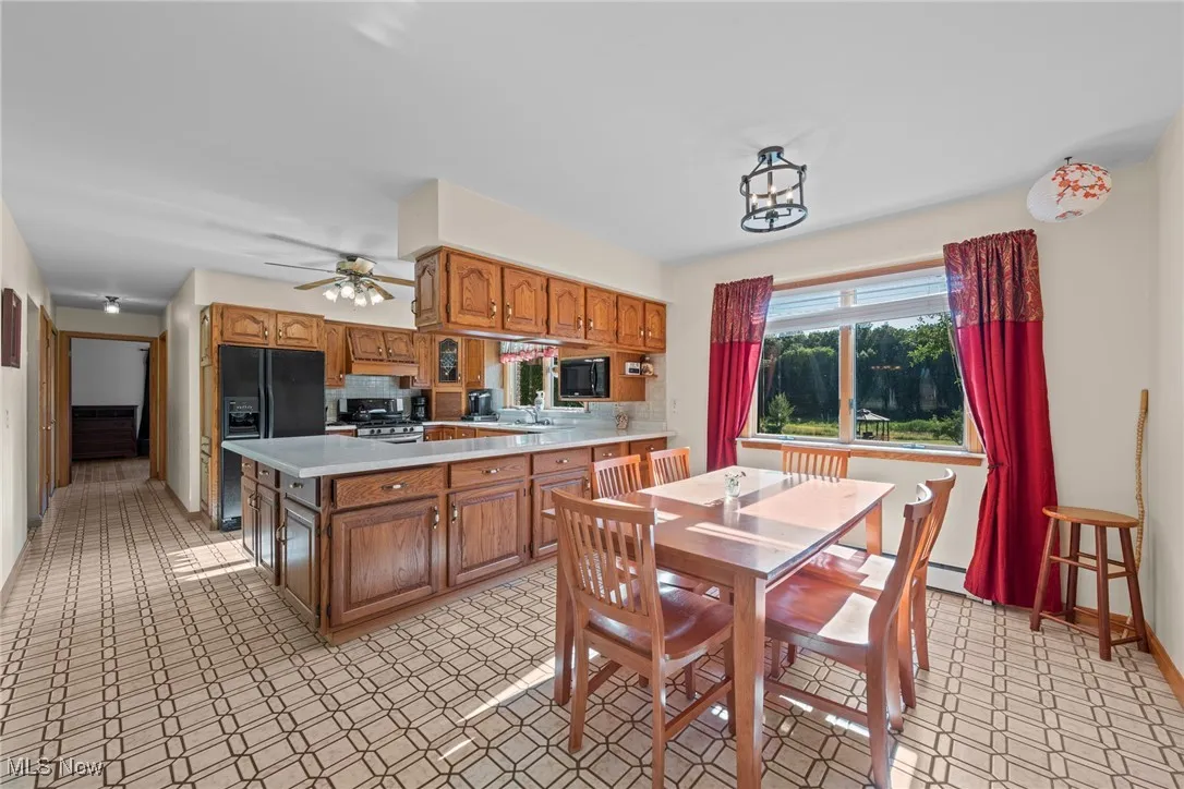 Kitchen with light countertops, brown cabinetry, stainless steel gas range oven, a peninsula, and black fridge with ice dispenser