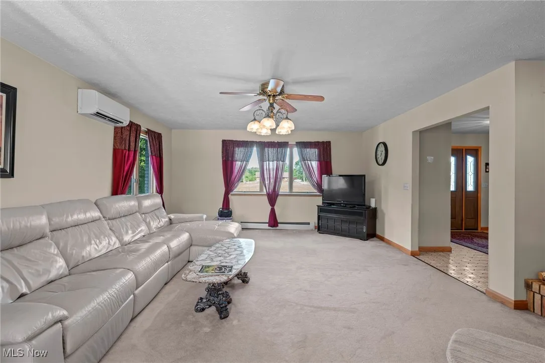 Living area with light colored carpet, a textured ceiling, ceiling fan, a baseboard radiator, and an AC wall unit