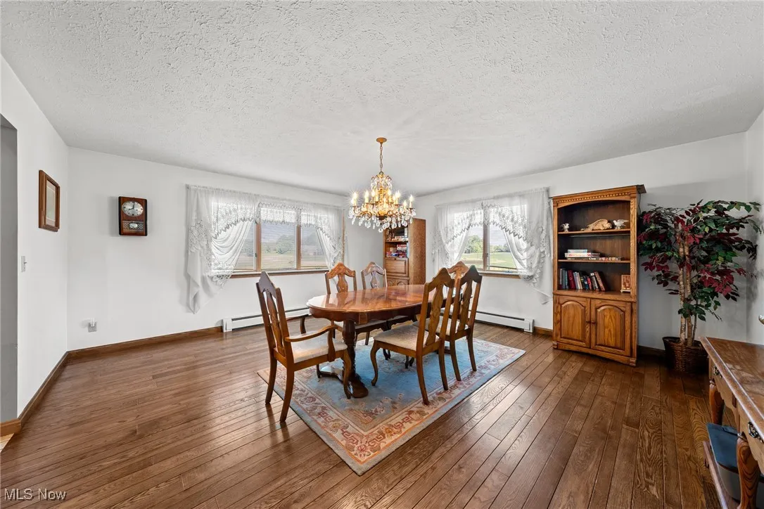 Dining area with plenty of natural light, a textured ceiling, a chandelier, dark wood-style floors, and baseboard heating