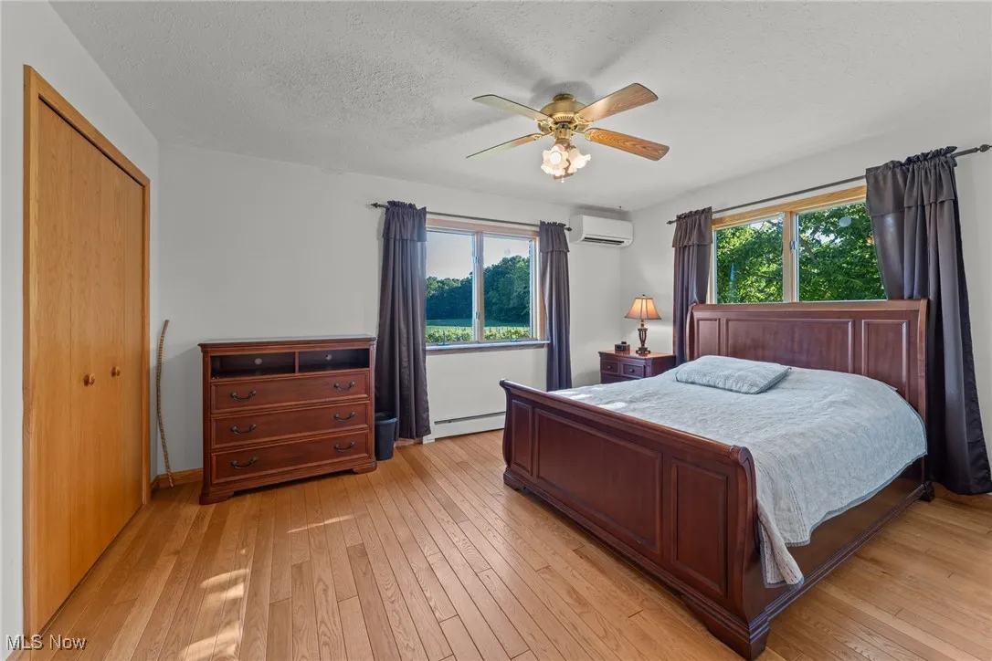 Bedroom with multiple windows, a textured ceiling, light wood-style flooring, a wall unit AC, and a baseboard heating unit