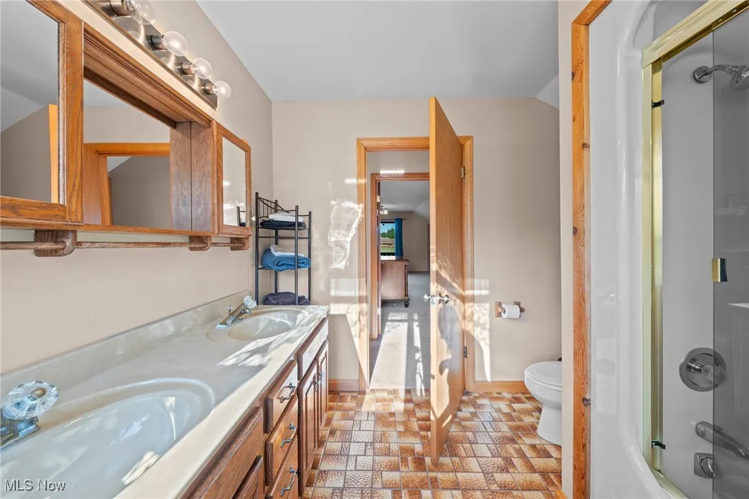 Bathroom featuring double vanity, vaulted ceiling, shower / bathtub combination, and stone finish floors