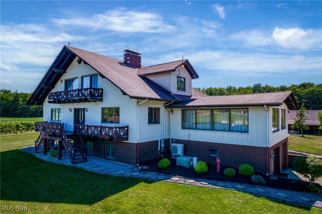 Back of property with a balcony, brick siding, a lawn, stairs, and a chimney