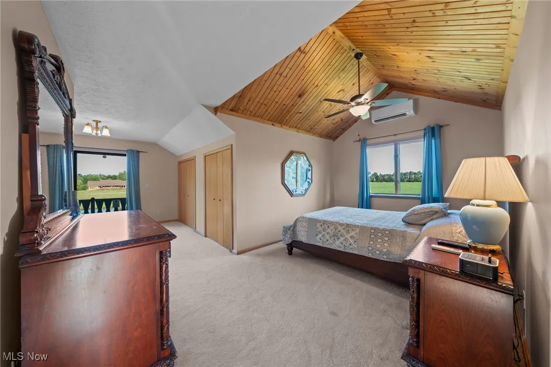 Carpeted bedroom with lofted ceiling, wooden ceiling, multiple windows, ceiling fan, and a wall unit AC