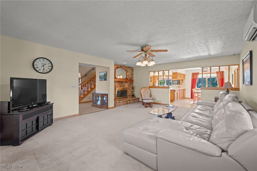 Living room with light colored carpet, a wall mounted air conditioner, ceiling fan, a textured ceiling, and a fireplace