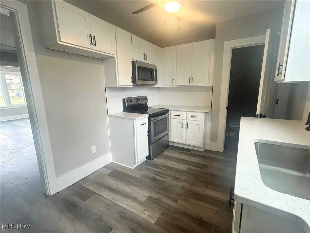 Kitchen featuring stainless steel appliances, white cabinets, dark wood-style floors, light stone countertops, and tasteful backsplash