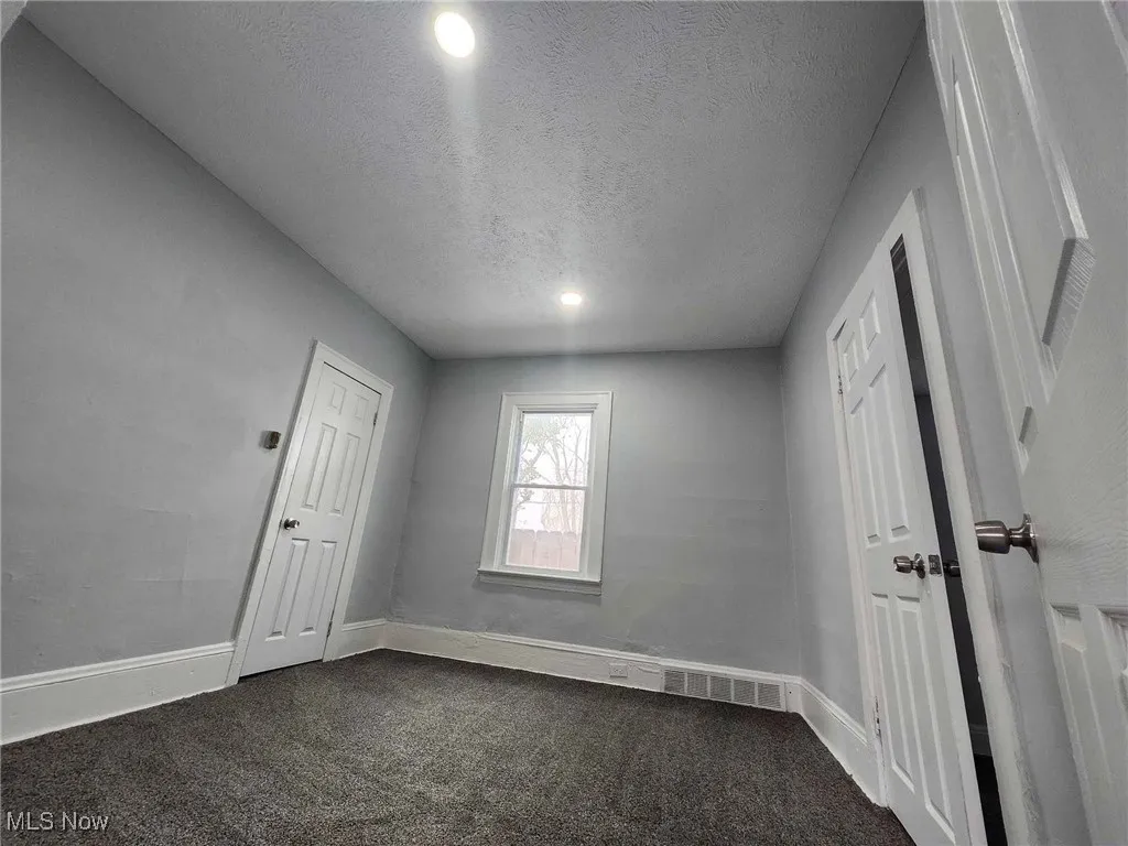 Unfurnished bedroom featuring a textured ceiling, dark carpet, and recessed lighting