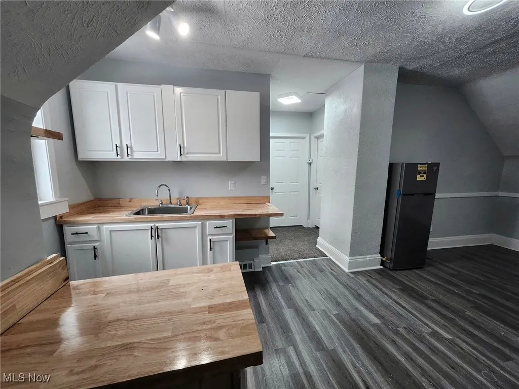 Kitchen featuring a textured ceiling, wooden counters, white cabinets, dark wood-style floors, and freestanding refrigerator