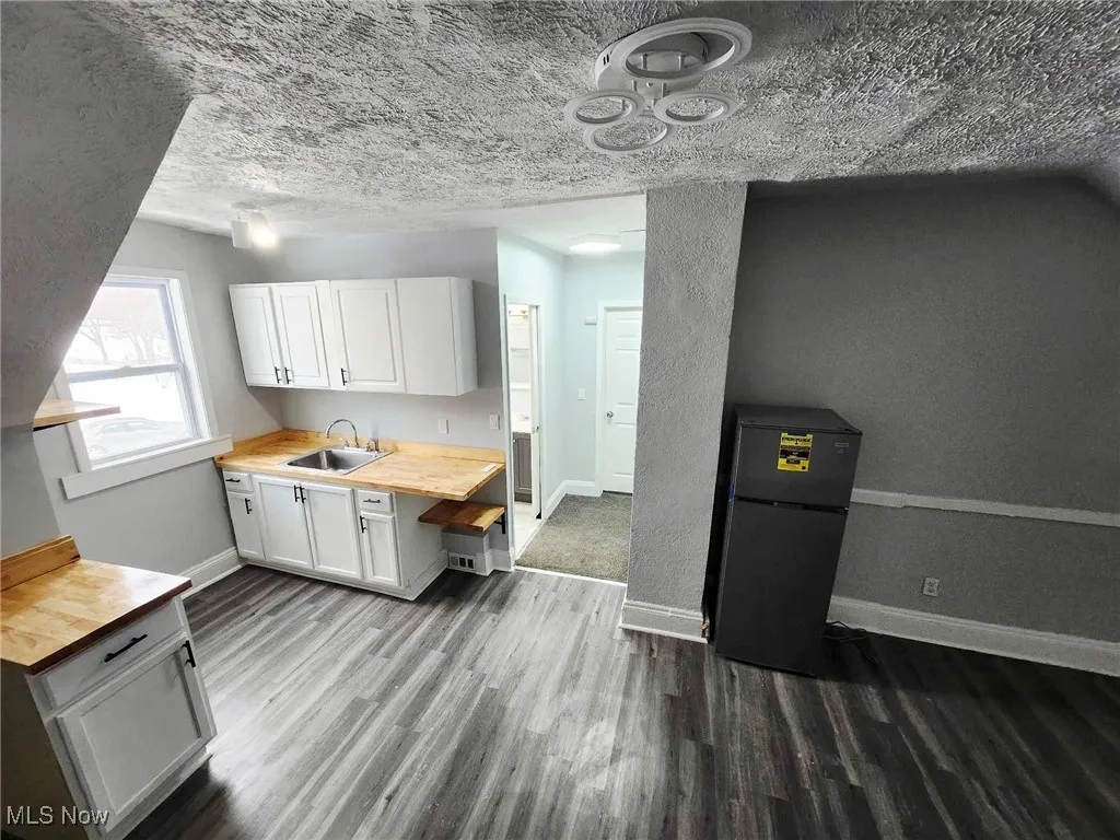 Kitchen featuring wooden counters, dark wood finished floors, white cabinets, refrigerator, and a textured ceiling