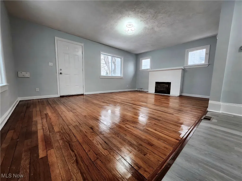 Unfurnished living room featuring wood-type flooring, plenty of natural light, a fireplace, and a textured ceiling