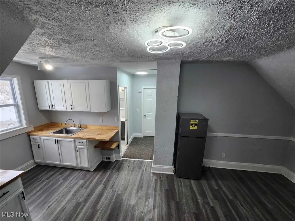 Kitchen featuring black refrigerator, dark wood finished floors, white cabinetry, a textured ceiling, and wooden counters