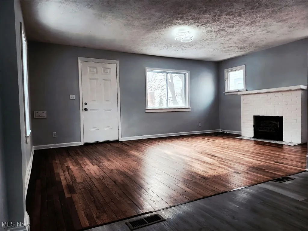 Unfurnished living room with dark wood-style floors, a textured ceiling, and a fireplace