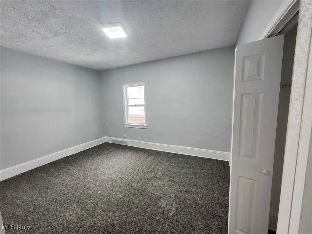 Unfurnished room featuring dark carpet and a textured ceiling