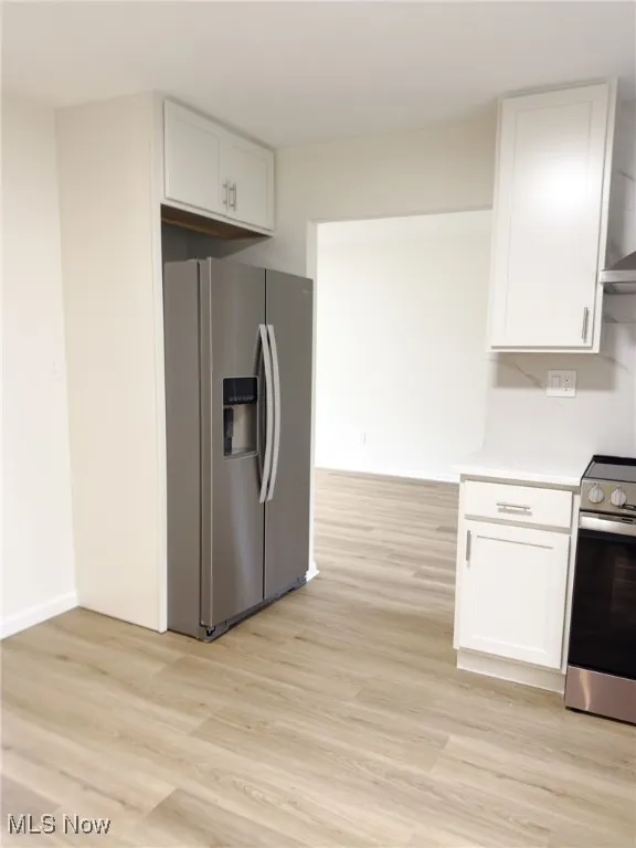 Kitchen with appliances with stainless steel finishes, light wood-style floors, white cabinets, and wall chimney exhaust hood